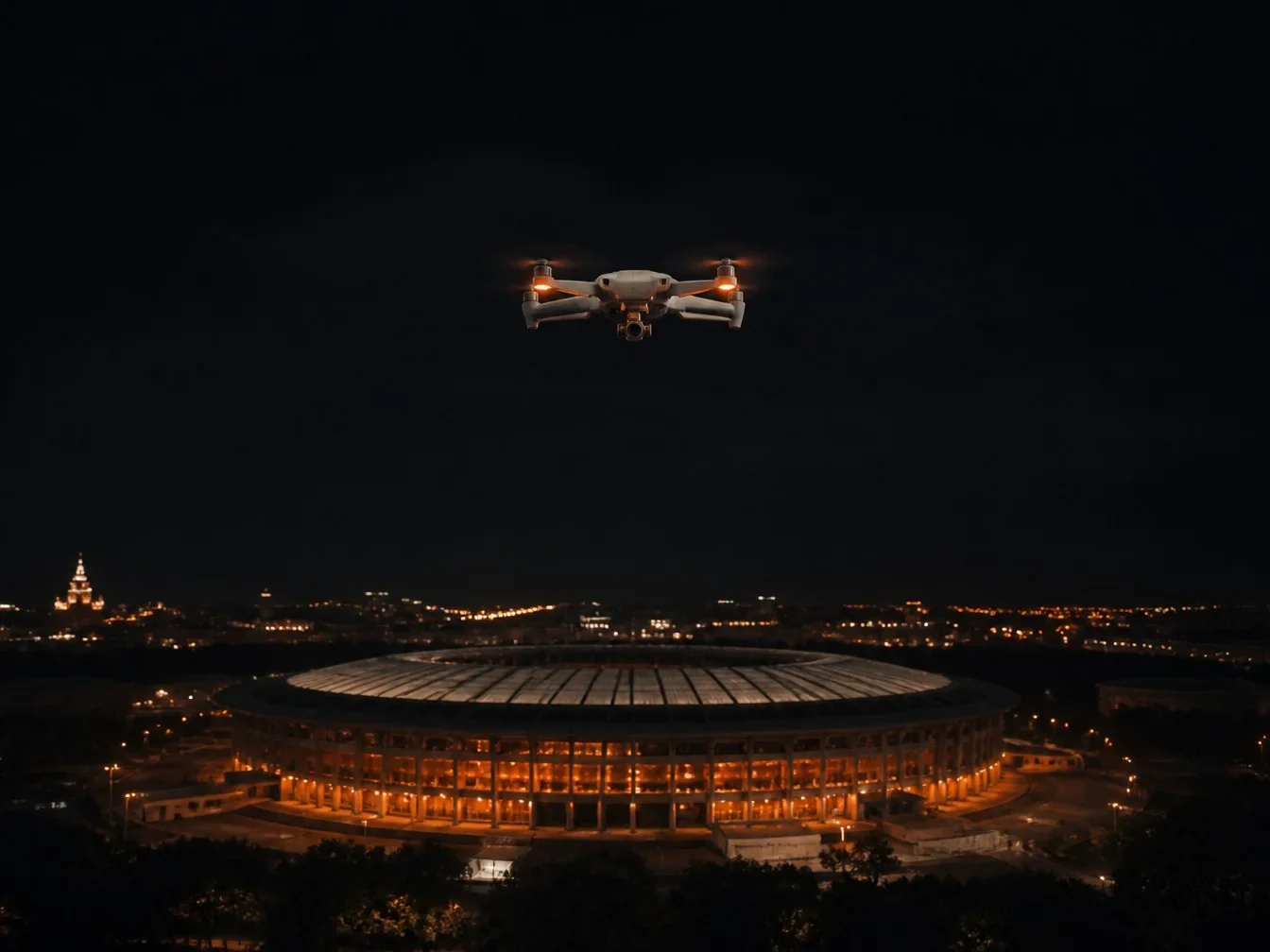 Standard camera drone hovering high above a stadium at night
